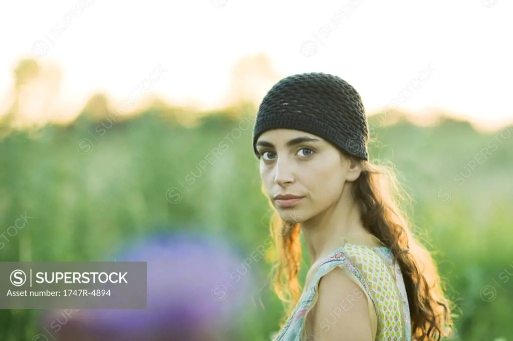 Young woman outdoors, looking over shoulder at camera