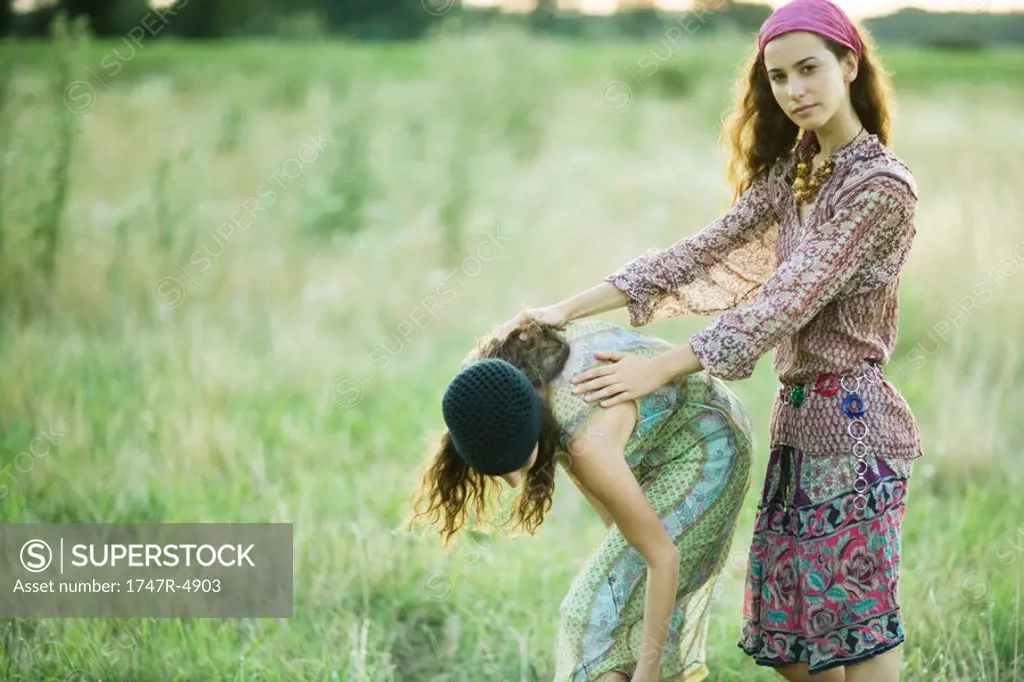 Young women in field, one bending over while the other holds her back