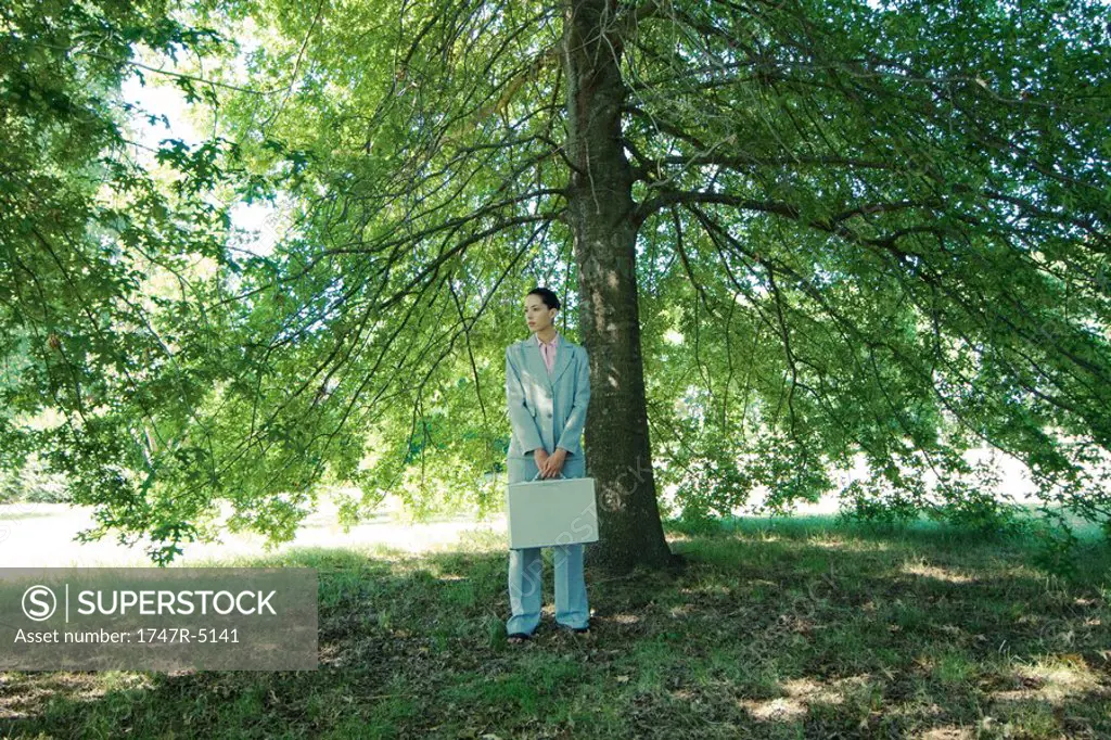 Businesswoman standing under tree, holding briefcase