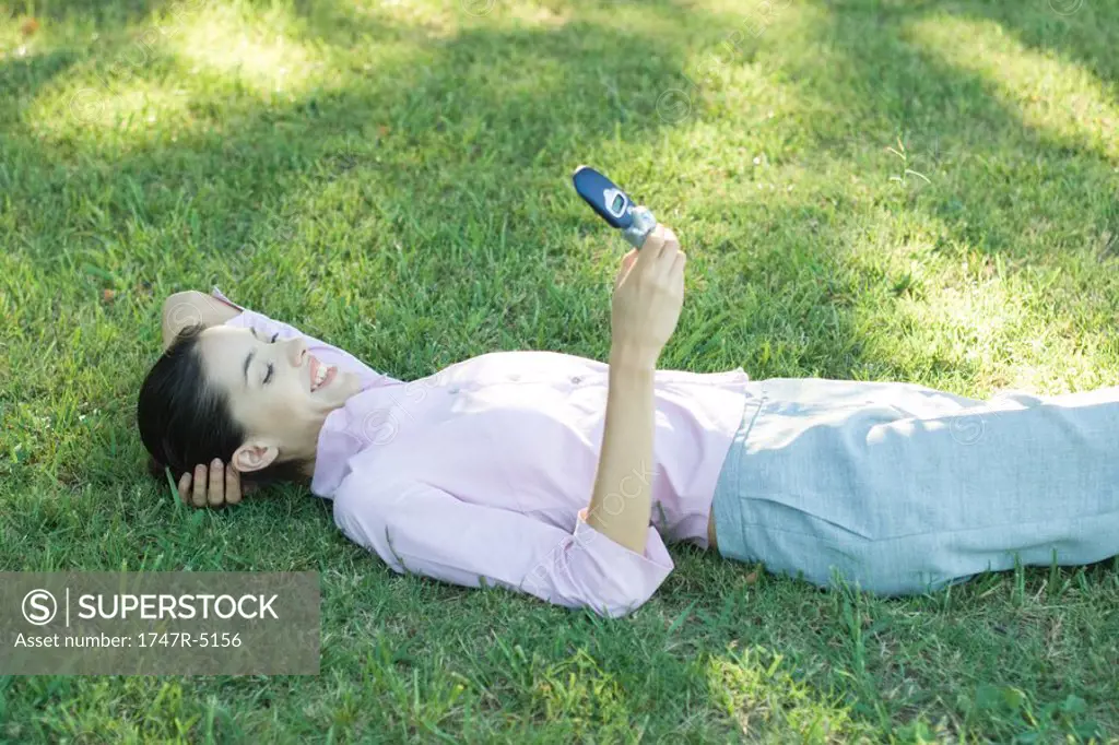 Businesswoman lying in grass, looking at cell phone, smiling