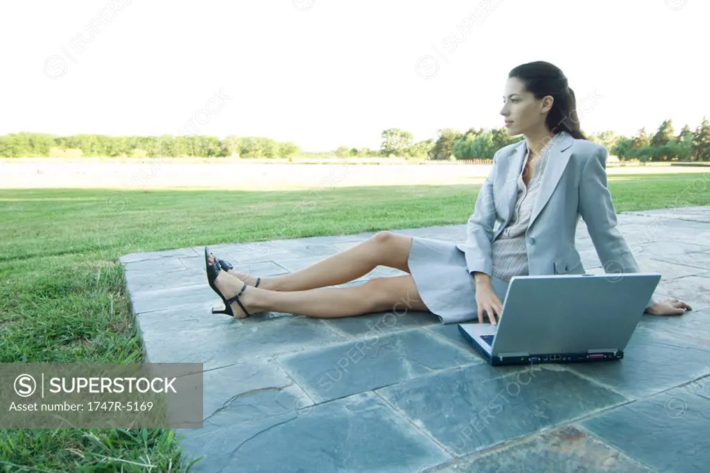 Businesswoman sitting on patio with laptop, looking away