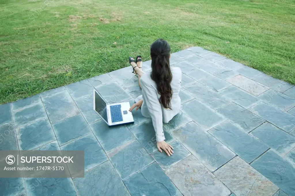 Businesswoman sitting on patio with laptop, looking away, high angle, rear view