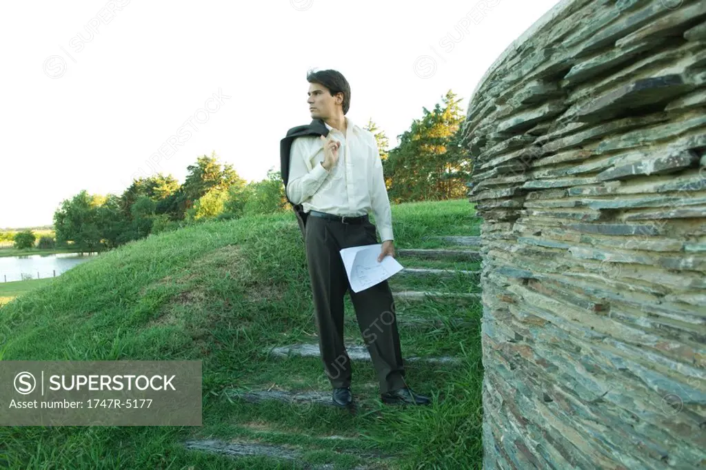 Man standing near stone wall, holding blueprints