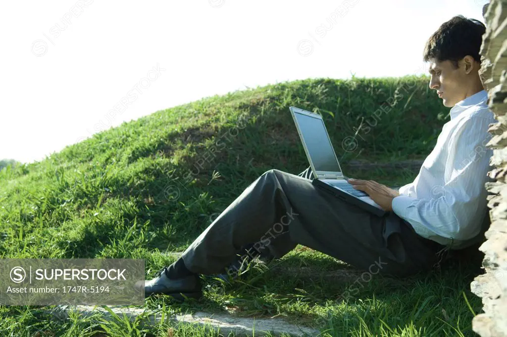 Businessman sitting on ground, using laptop