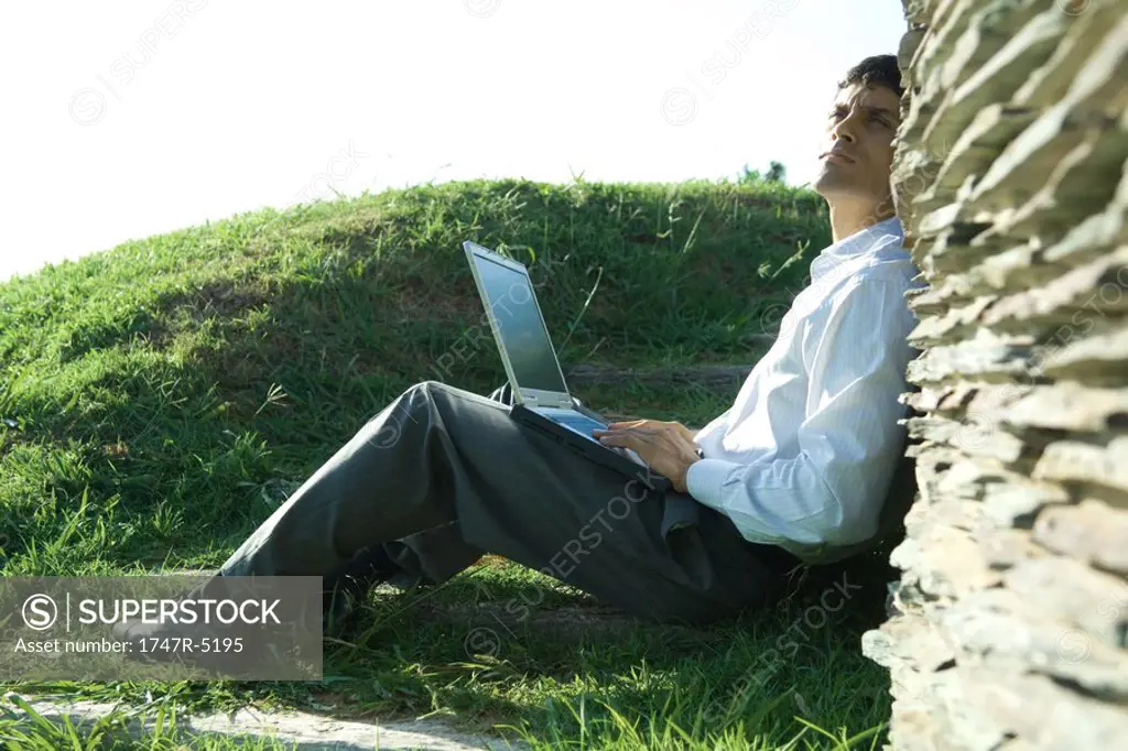 Businessman sitting on ground, using laptop, looking up