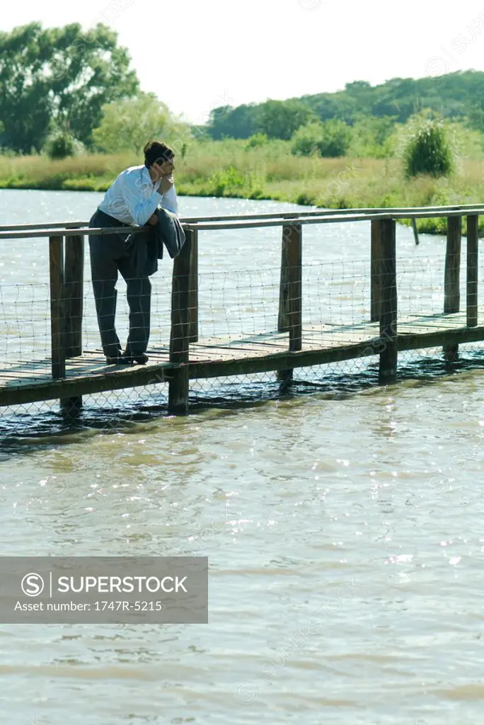 Businessman on wooden footbridge over lake, looking away