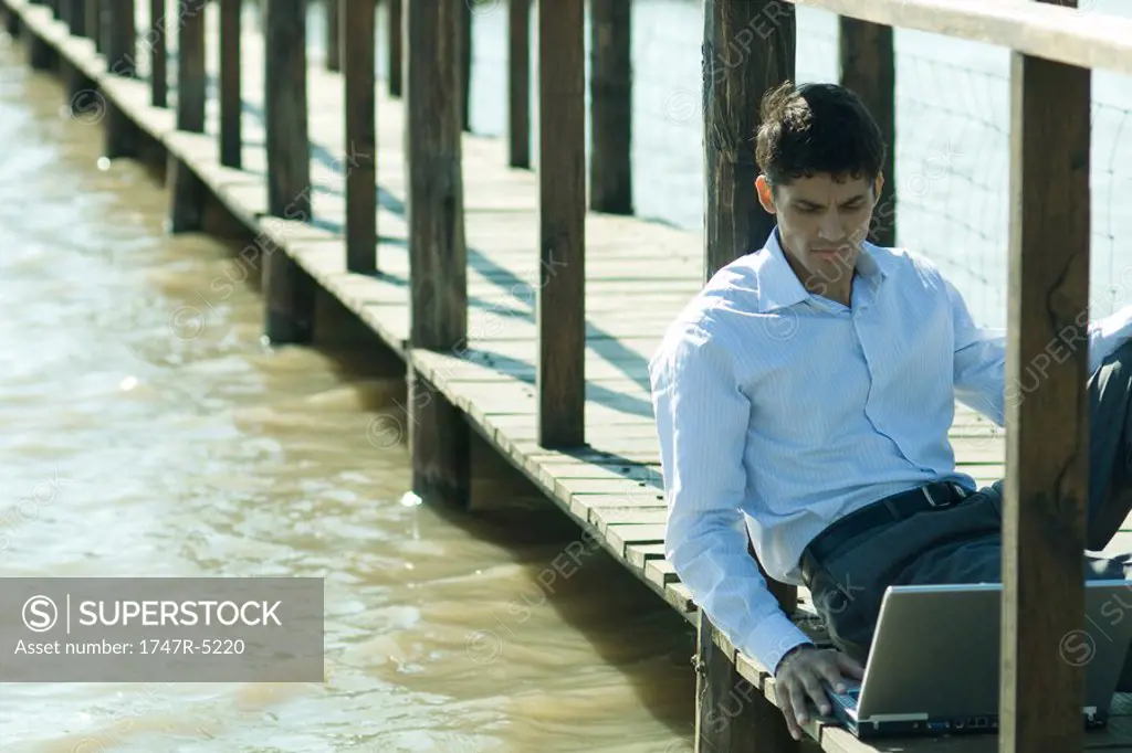 Businessman on wooden footbridge over lake, using laptop