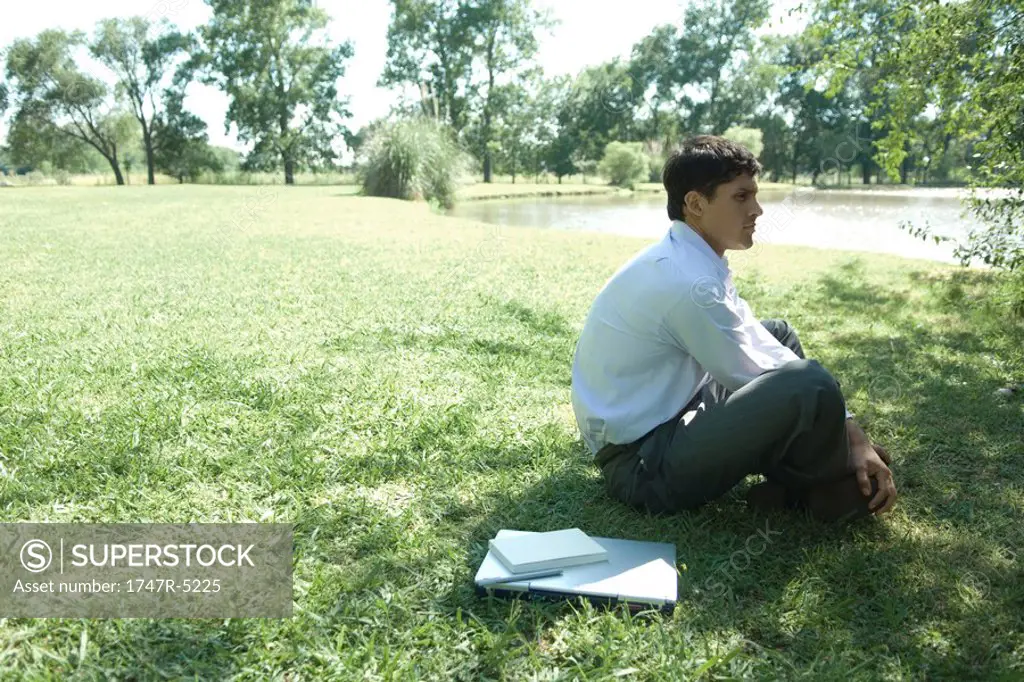 Businessman sitting on grass, laptop closed by side