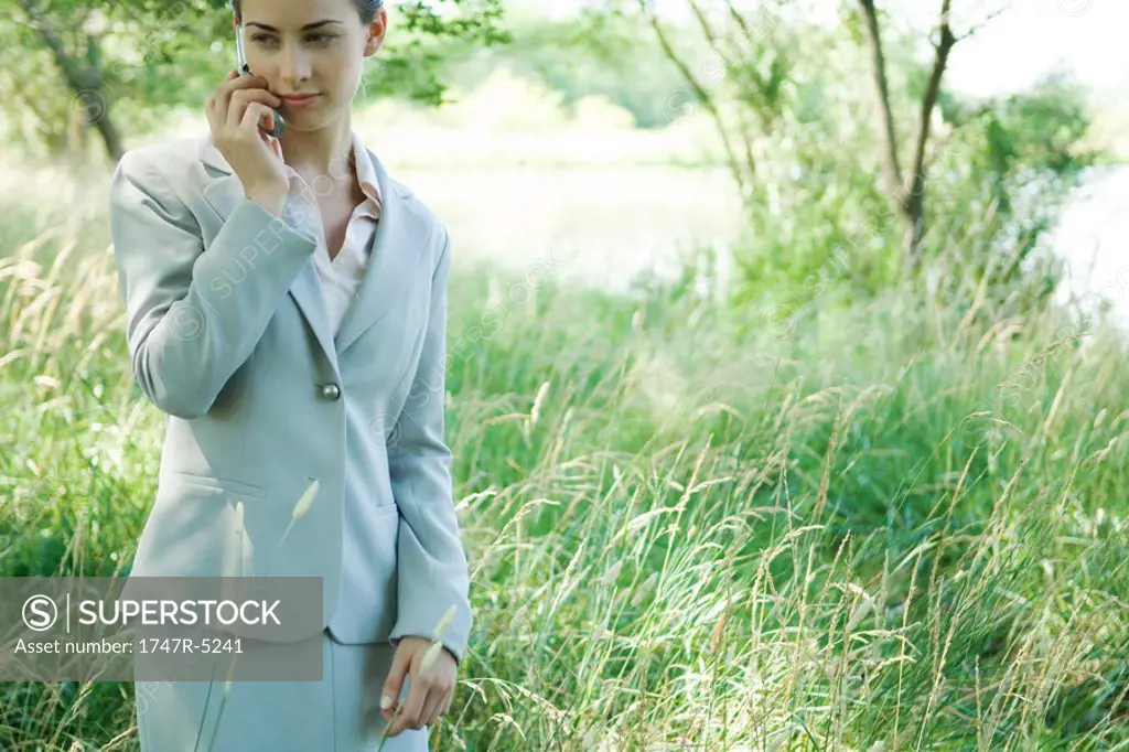 Businesswoman standing in field, using cell phone