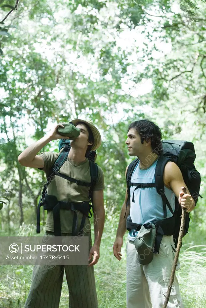 Hikers standing in woods, one drinking from water bottle