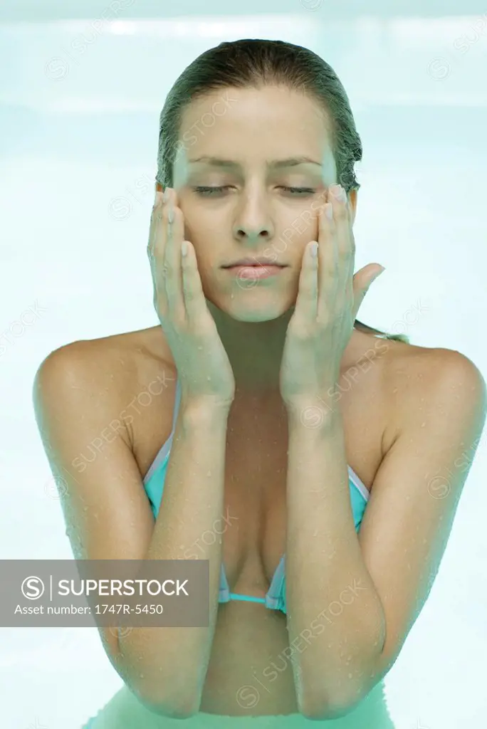 Young woman in pool, eyes closed, hands on side of face