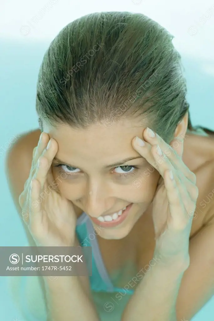 Young woman in pool, hands on side of face, smiling at camera