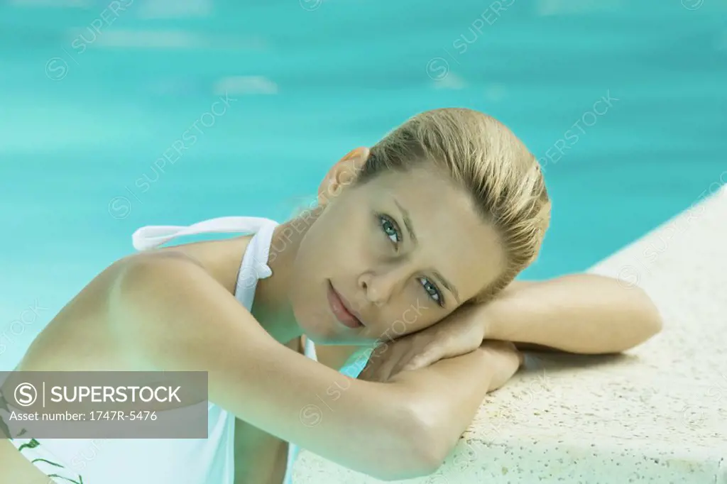 Woman resting head on edge of pool, looking at camera