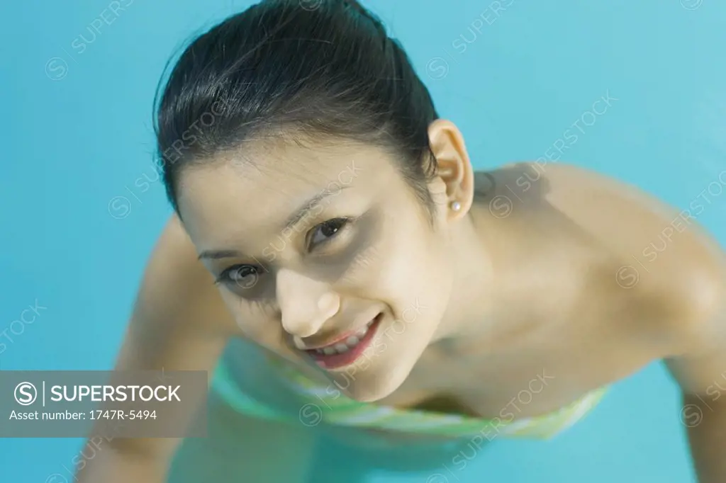 Young woman in pool wearing bikini, looking up at camera, close-up, high angle view