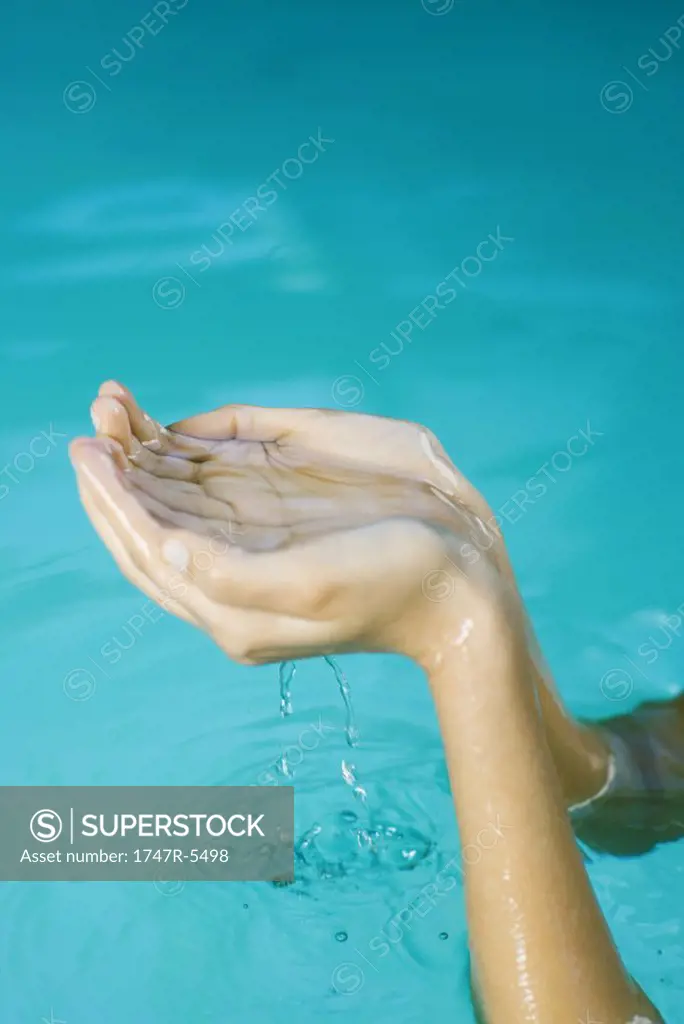 Young woman holding up cupped hands full of water, cropped view