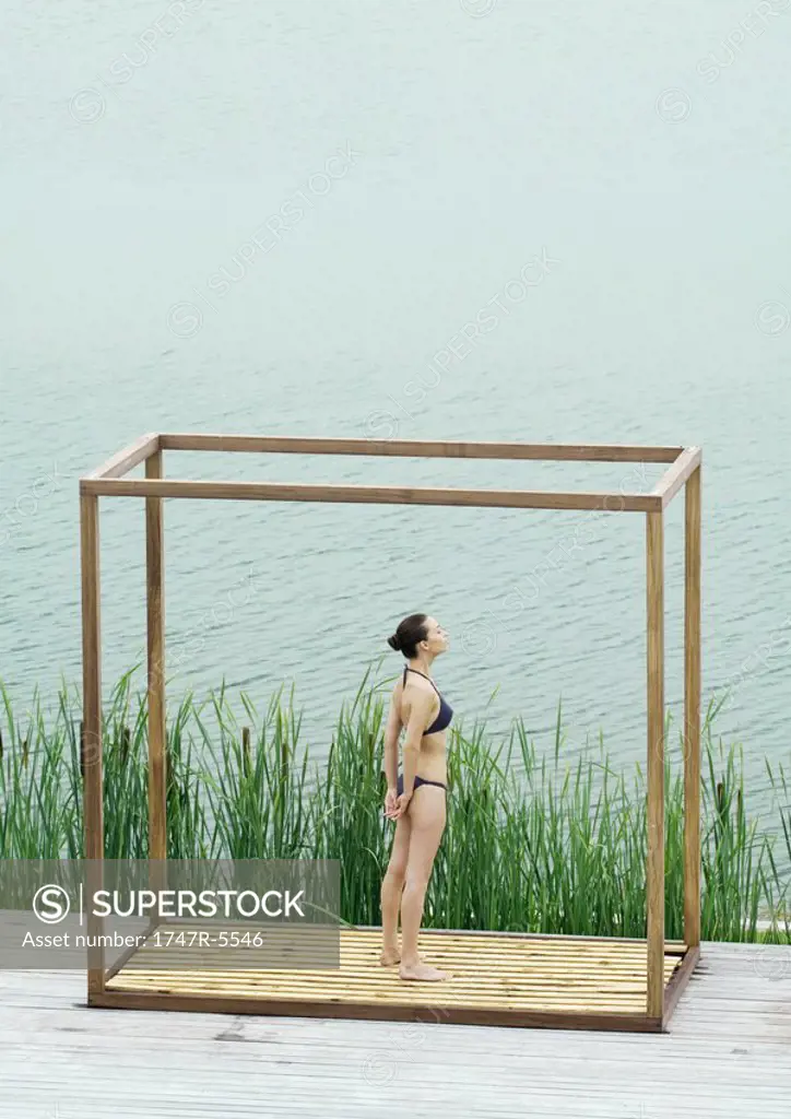Young woman standing inside square structure, next to body of water