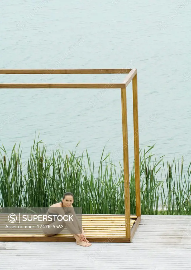 Woman sitting in square structure, body of water in background