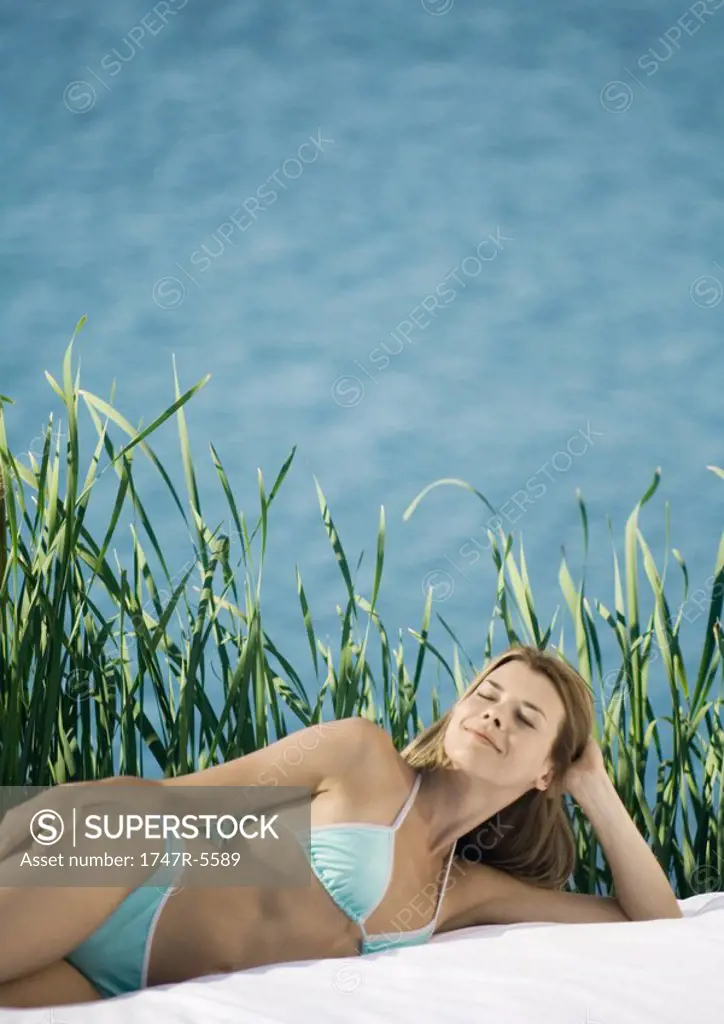 Woman lying on side, water and reeds in background