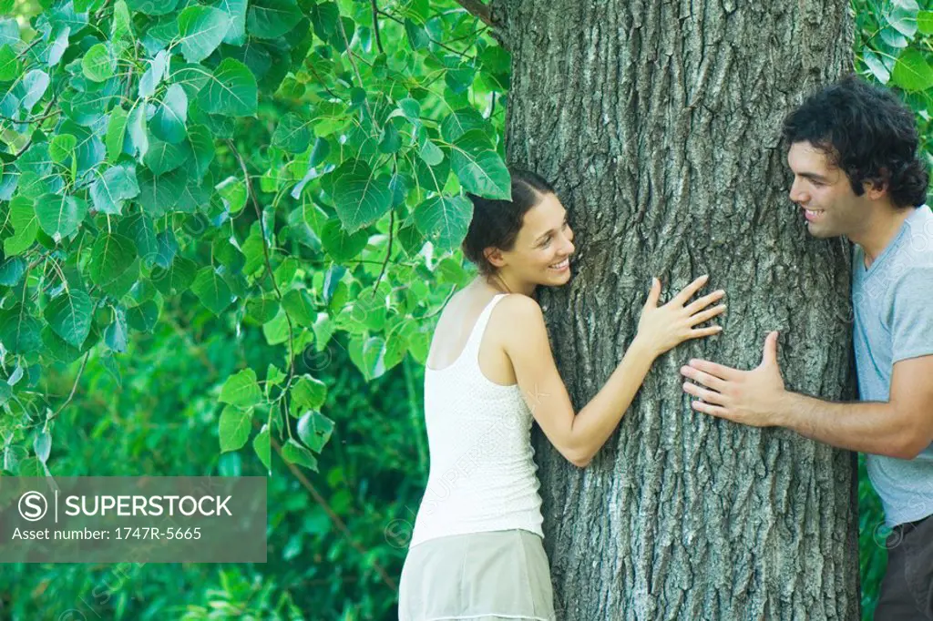 Couple looking at each other from around tree