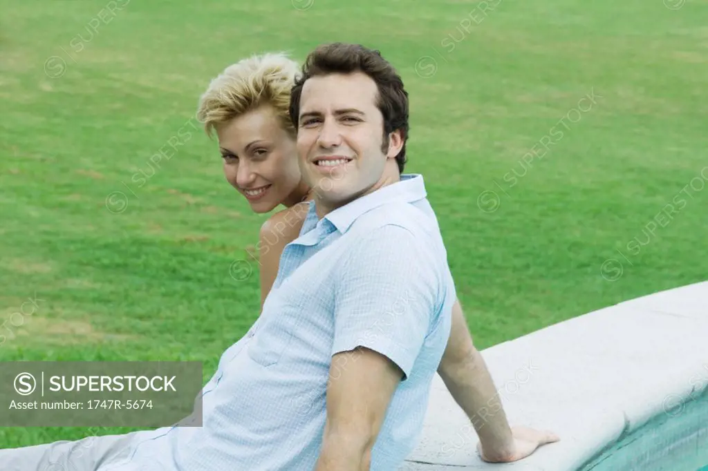 Couple sitting by pool together, smiling at camera