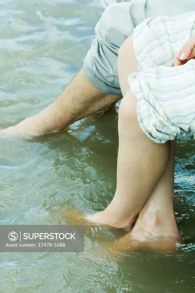 Couple dangling feet into water, cropped view