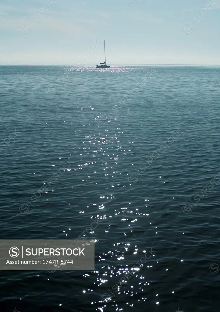 Sun glittering on surface of lake, sail boat in background
