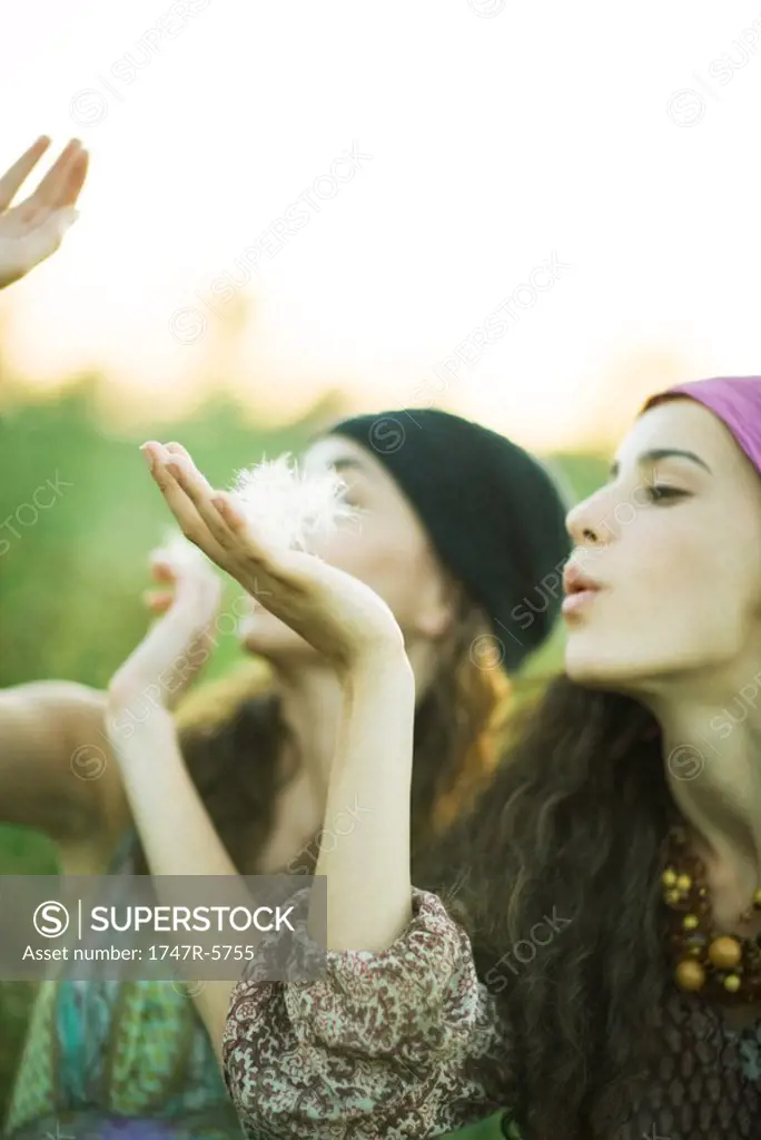 Young hippie women blowing dandelion seeds