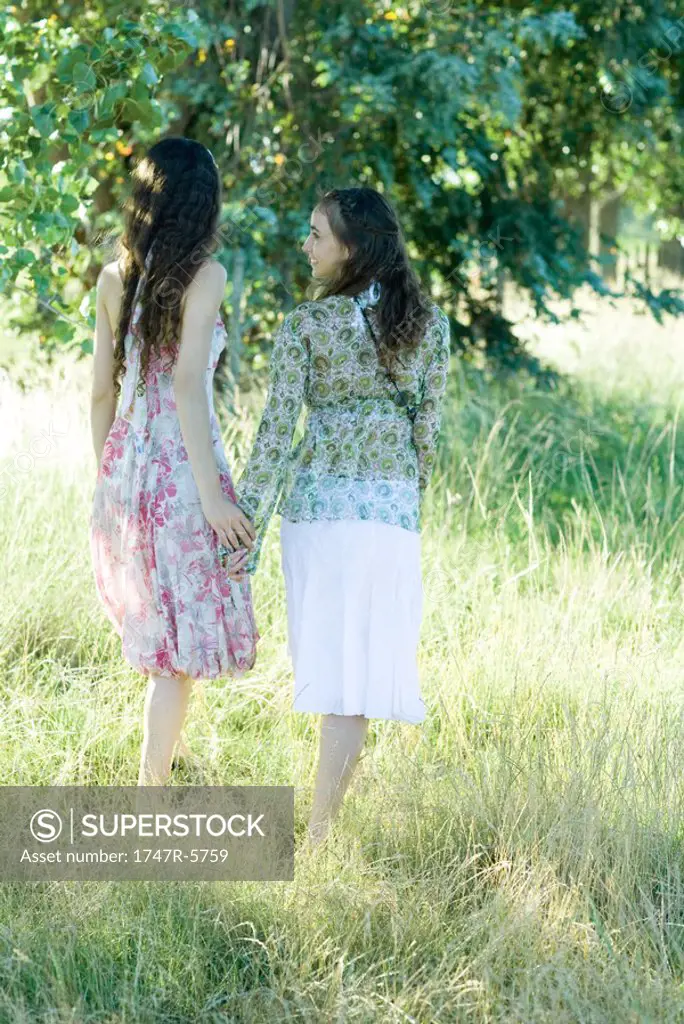 Young hippie women walking through field, holding hands