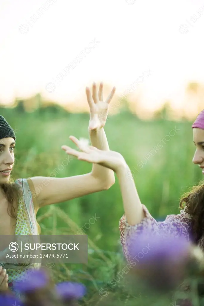 Young hippie women, hands up catching dandelion seed heads