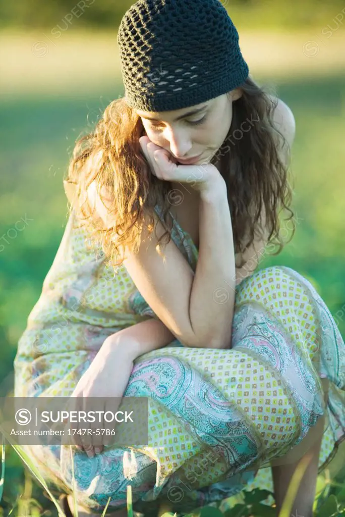 Young hippie woman crouching in grass, looking down