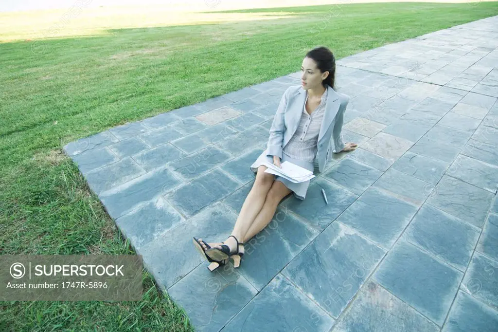 Businesswoman sitting on ground on patio, holding documents