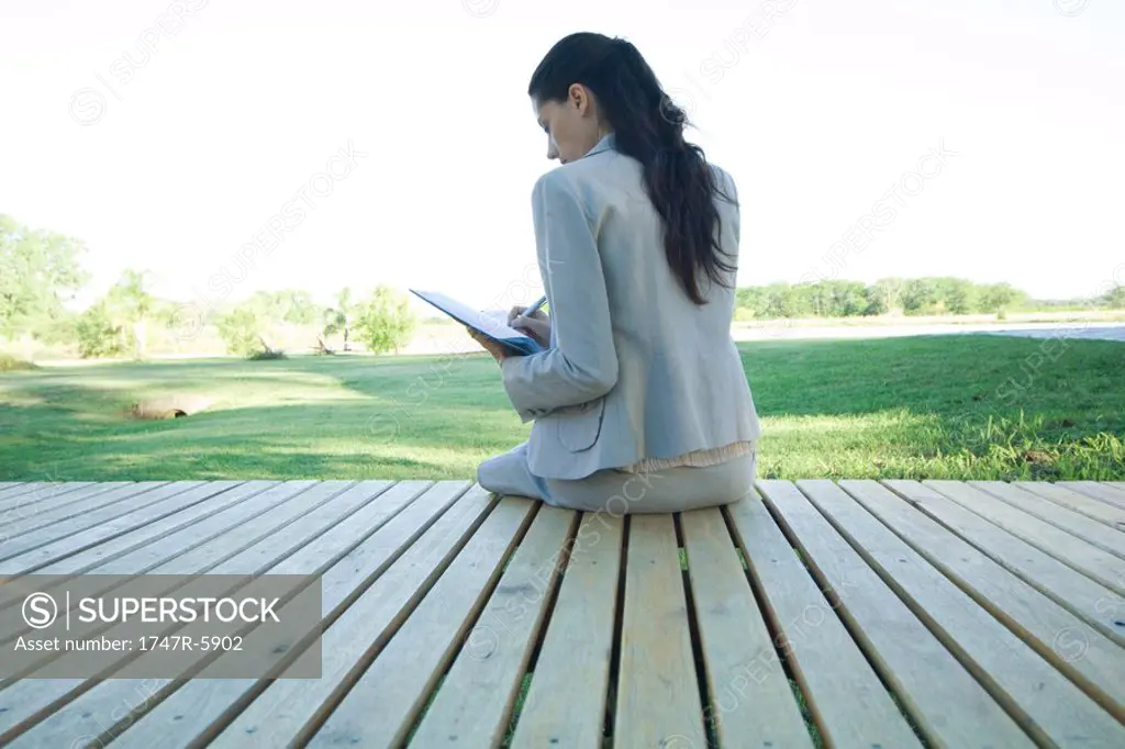 Businesswoman sitting on decking, writing