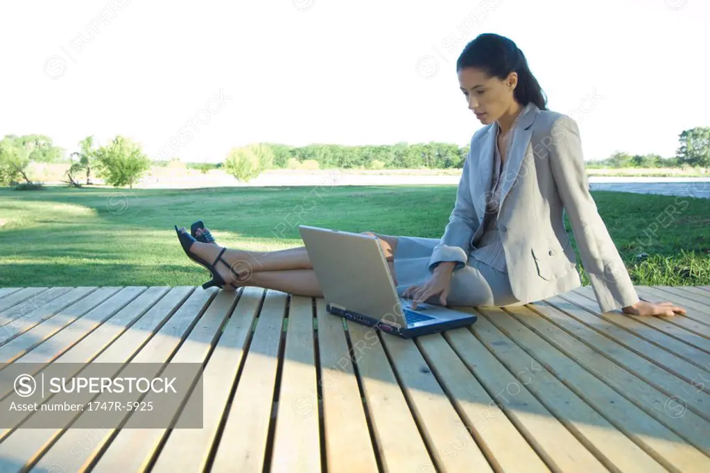 Businesswoman sitting on decking, using laptop