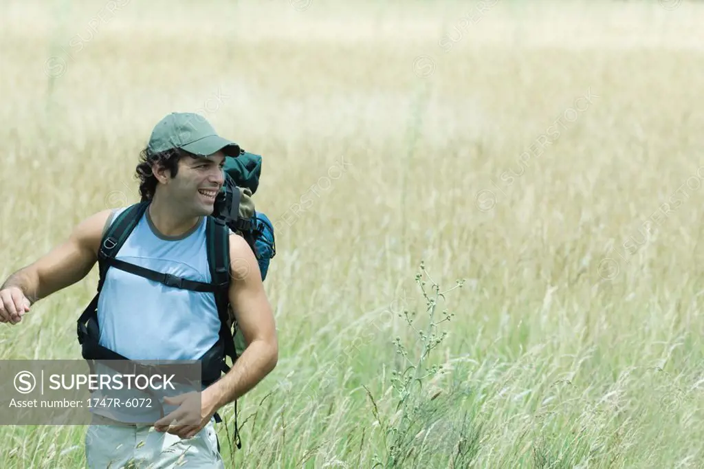 Young male hiker walking through field, looking away, smiling