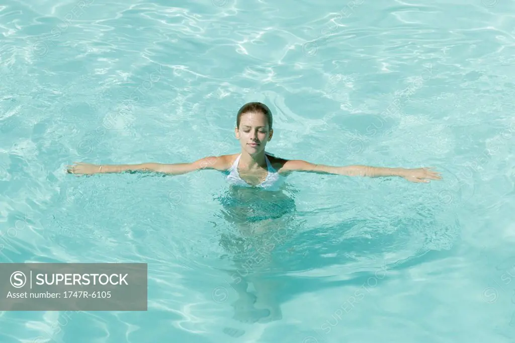 Young woman in pool with arms out and eyes closed