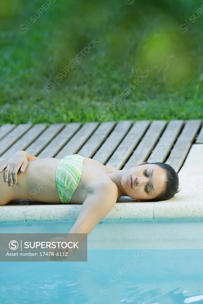 Young woman lying by edge of pool, holding water in cupped hand