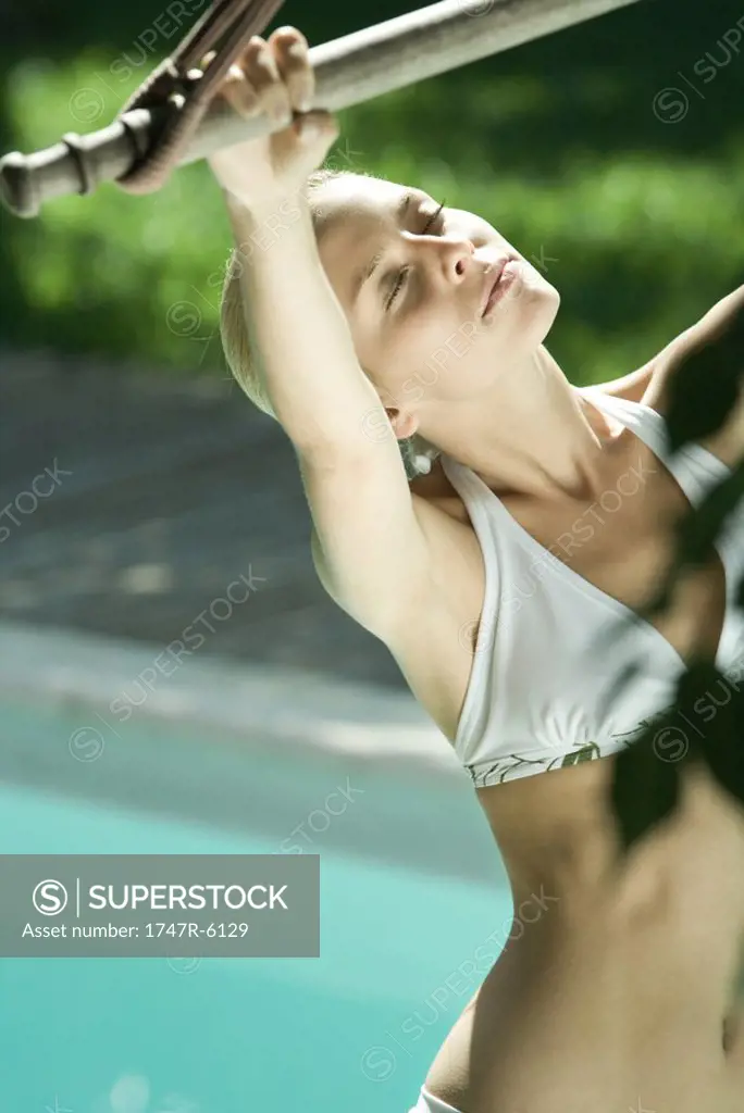 Young woman in bikini, holding onto bar, pool in background