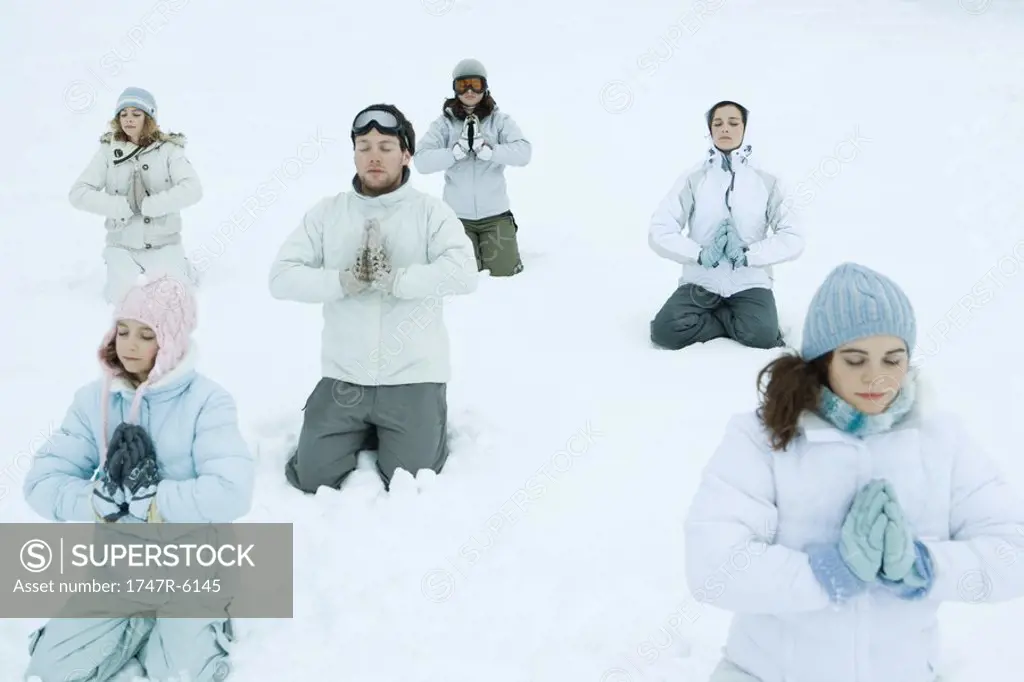 Group kneeling in snow with hands clasped and eyes closed