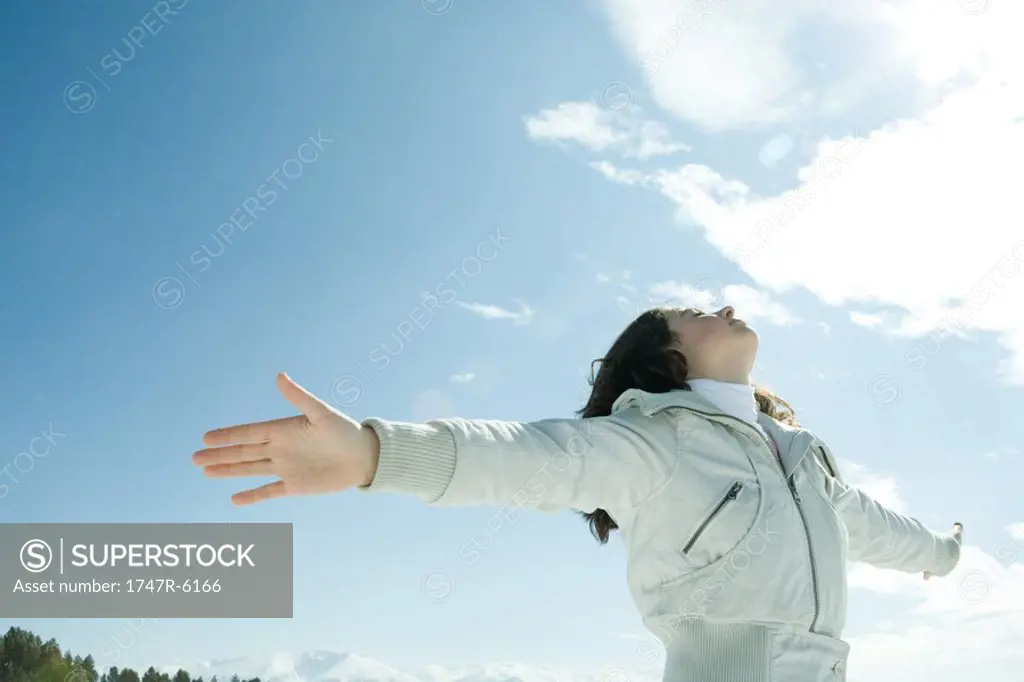 Teen girl standing in snowy landscape, arms raised to sun