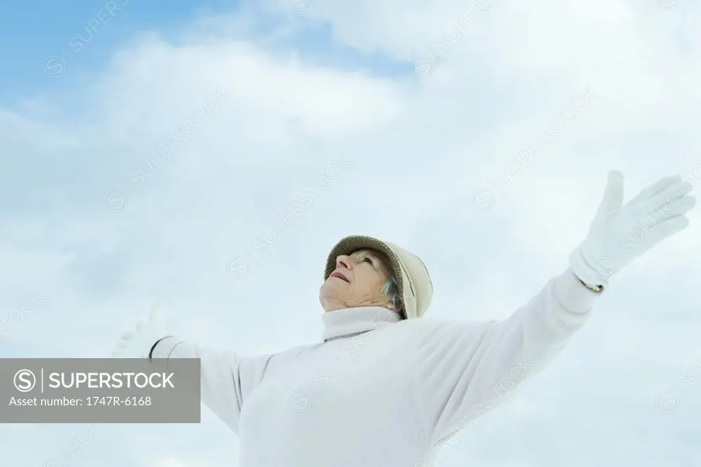 Senior woman standing with arms out, looking up at sky