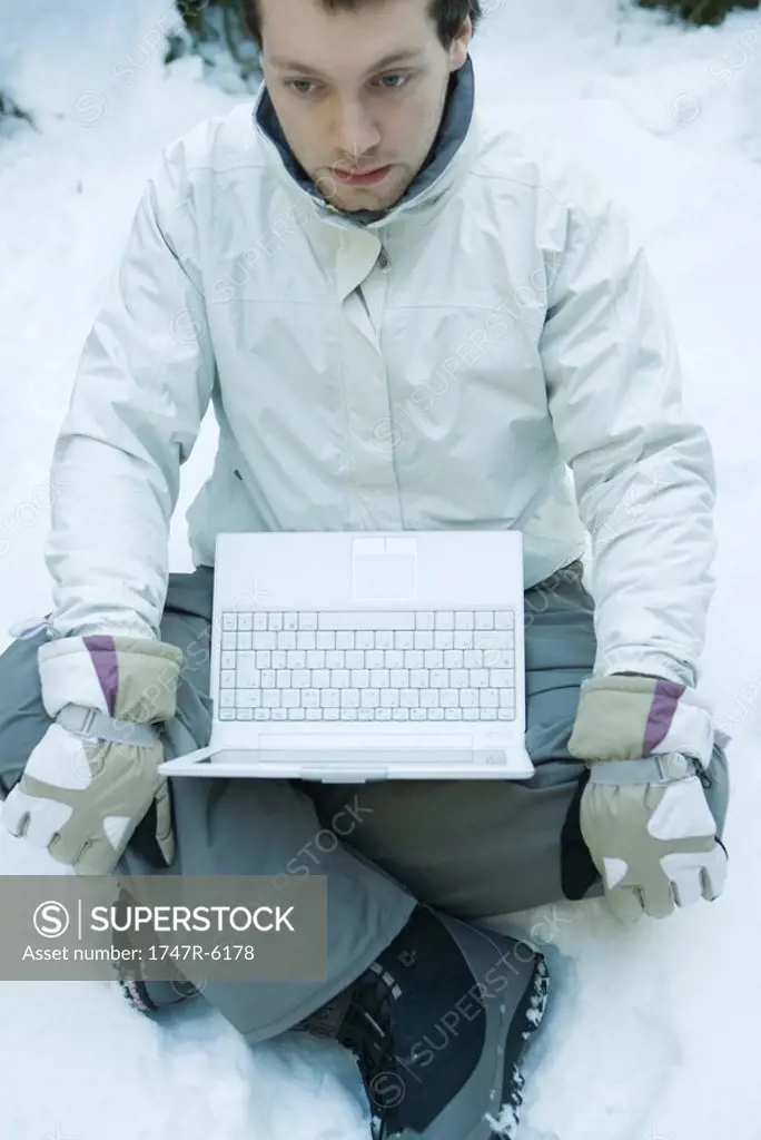 Young man sitting in snow, laptop on lap