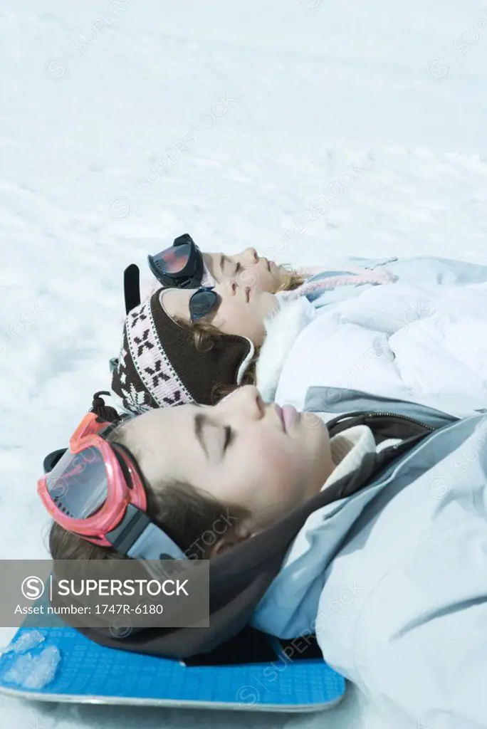 Three friends lying on snow together, eyes closed