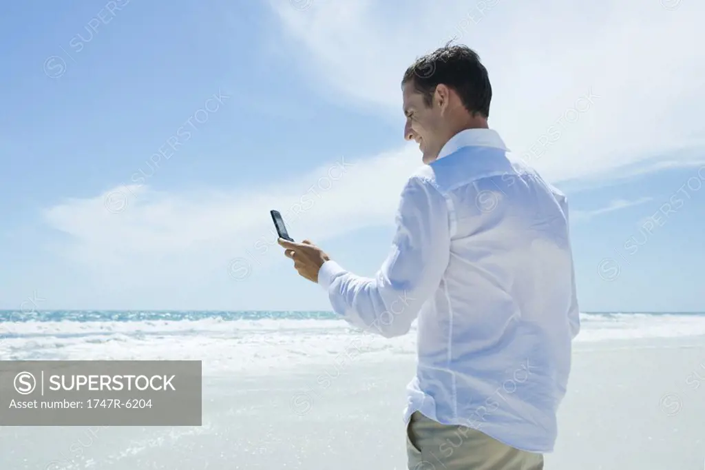 Businessman dialing cell phone on beach