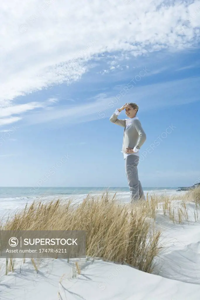 Woman standing on dune, shading eyes, smiling