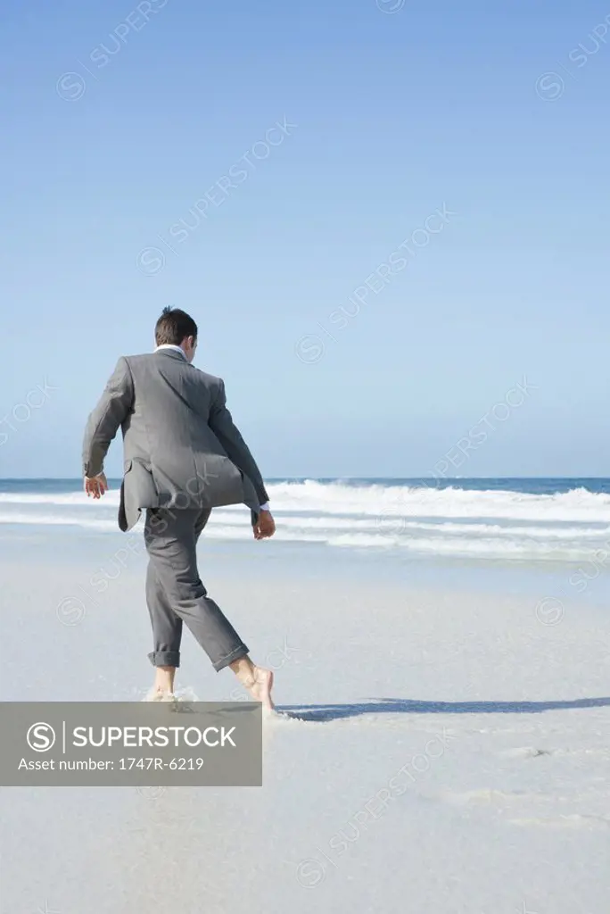 Barefoot businessman walking across beach