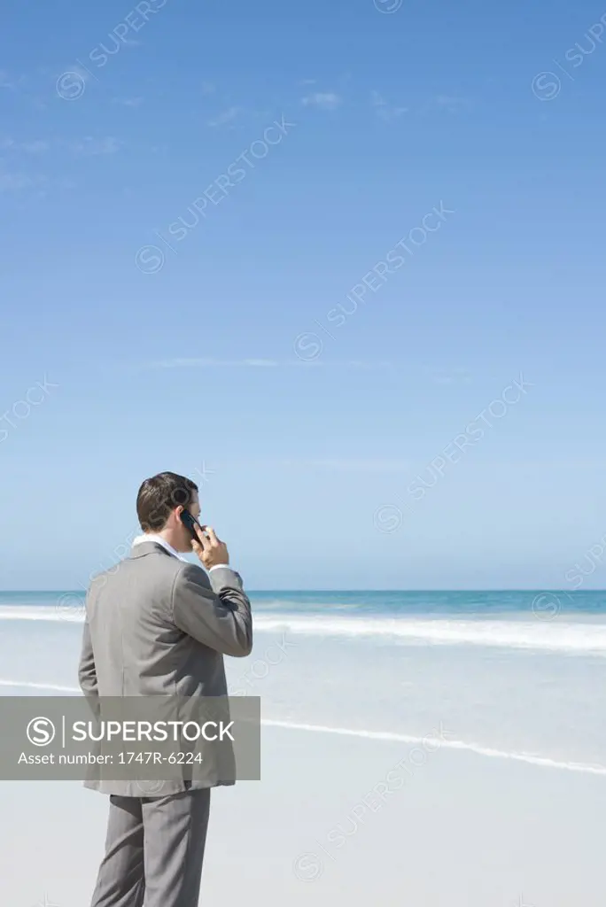Businessman standing on beach, using cell phone