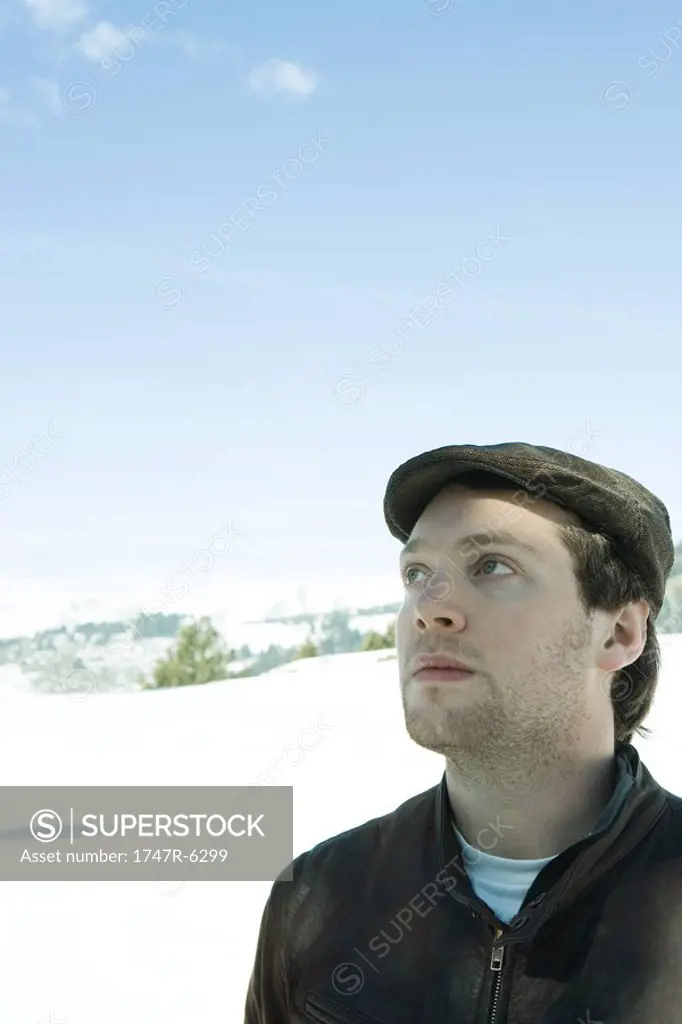 Young man wearing hat in snowy landscape, looking up