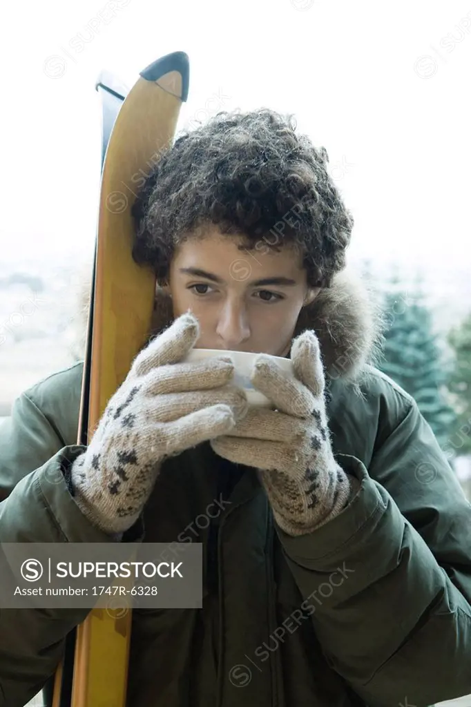 Teen boy with skis drinking warm drink