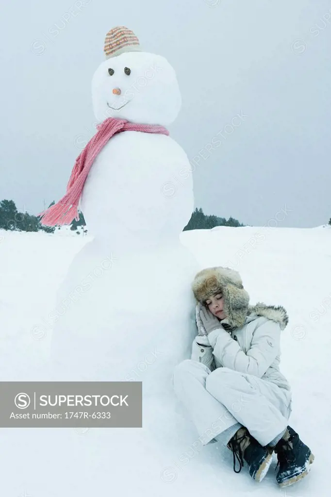 Teen girl leaning against snowman, sleeping