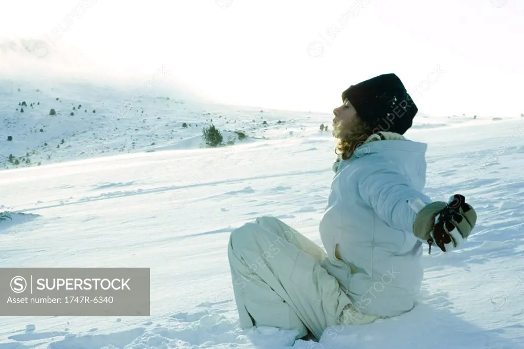 Teen girl sitting on snow, eyes closed and arms out to sides